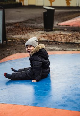 Mavi şişirilebilir trambolinde oturan, kar tulumu giymiş bir çocuğun muzip gülümsemesi. Oyun parkındaki bir hava fedaisine kurnaz bir bakışla gülen çocuk. Neşeli gülüşü ya da ifadesi olan yorgun bir çocuk.
