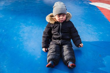 Mavi bir trambolinde oturan kızgın çocuk. Sert bakışlı sinirli bir çocuk, havalı bir fedainin üzerinde, meydan okuyan bir bakışla oturuyor. Serseri çocuk sert bir ifadeyle bakıyor anlaşmazlıkta ya da muhalefette