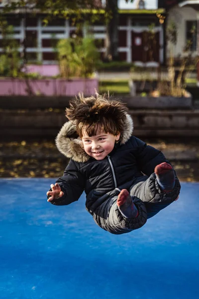 Joyful kid flying sit while jumping pole vault. Cheerful boy or kid sitting in the air with straight legs. Free fall of a preschooler fluttering on blue bouncer. Boy happiness and freedom concept - Malmo, Sweden