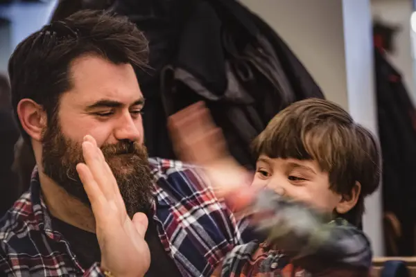 Relaxed guy with long beard and an excited boy exchange a high five indoor. Child give five to a long bearded man. Up top or slap hands between a happy child and a smiling man in a restaurant