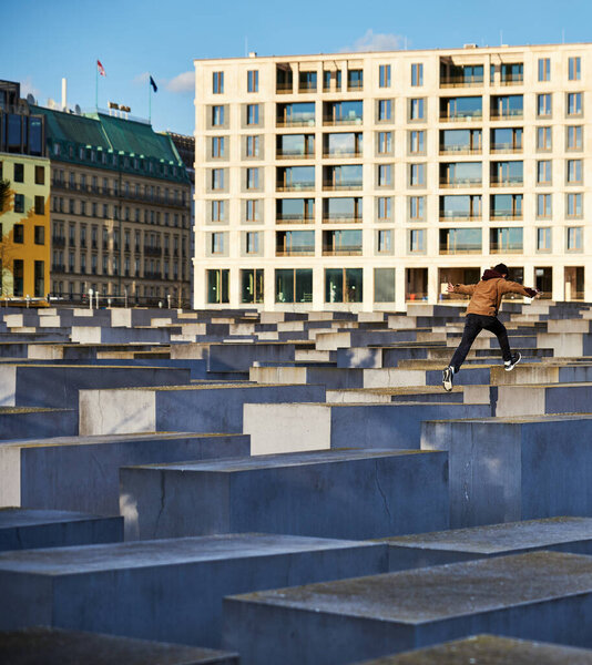 Kid jumping from one pillar to the other on Memorial to the Murdered Jews of Europe conveys concept of freedom. Child leaping between slabs on the Holocaust Memorial surrounded by a concrete cityscape