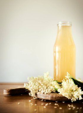 Baharın tadı. Önden görünüşlü Elder çiçeği, ahşap masada, beyaz Elder çiçekleriyle çevrili. Beyaz Elder veya Elderberry çiçekleri arasında mevsimlik yaşlı çiçek içeceği. Ev yapımı Sambucus içeceği