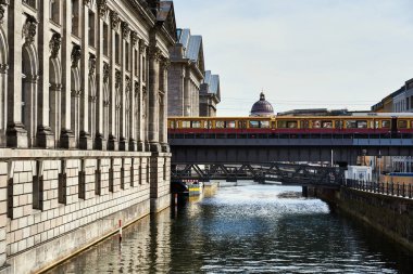 Berlin 'deki sarı metro, Spree nehri üzerindeki bir köprünün üzerinde durmuş ve kale kubbesi gözümüzün önündeymiş. Kanalın yanındaki tarihi eski bina metro köprüsünde duruyor. Berlin turizm konsepti