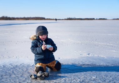 Küçük bir çocuk merakını keşfeder ve donmuş bir gölde oynar. Oyuncak bir kamera kullanırken karda diz çöker. Açık gökyüzü ve engin buzlu manzara merak, keşif ve yalnızlık temalarını vurguluyor.