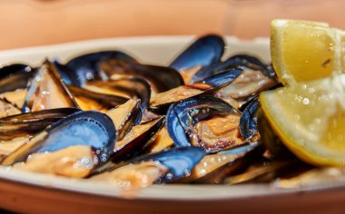 Parlak mavi kabuklu taze midyeler sulu limon dilimleriyle servis edilir, kıyı tatlarını, tazeliği ve okyanustan esinlenilmiş lezzetli bir yemek deneyimini çağrıştıran canlı bir deniz ürünleri tabağını vurgular.
