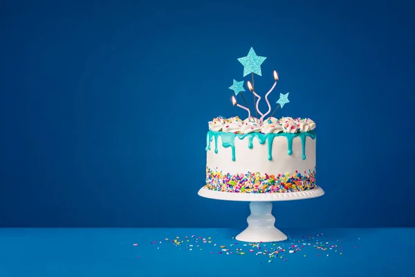 白色的生日蛋糕 带有时髦的焦糖滴和五彩斑斓的洒水 星光斑斓的顶灯和深蓝色背景的有趣的蜡烛 复制空间 — 图库照片
