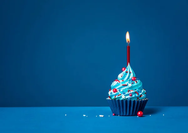 濃い青の背景に赤いスプリンクルとキャンドルブルーバタークリームの誕生日カップケーキ — ストック写真