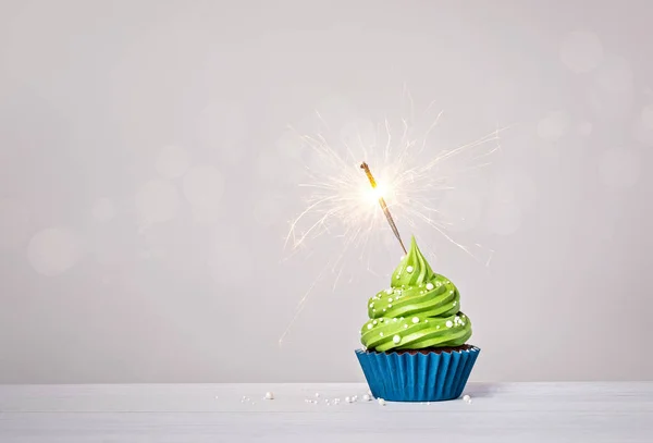 绿色生日杯蛋糕与奶油糖霜 蓝色杯蛋糕衬里 洒水和点燃的火花在浅灰白色的背景 复制空间 — 图库照片