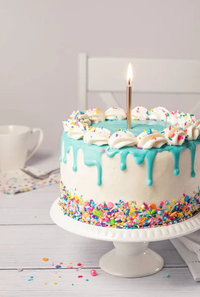 バニラバタークリームアイシング ライトゴールドの誕生日キャンドル カラフルな虹のコンフェッティスプリンクル 薄灰色の白いテーブル設定の背景にティールブルーのガナッシュドリップで誕生日ケーキを閉じます — ストック写真
