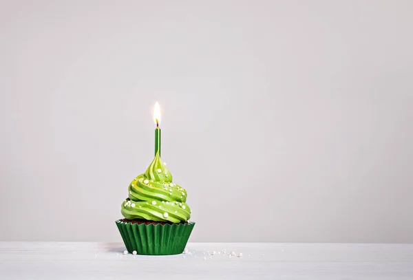 バタークリームアイシング スプリンクル ライトキャンドル付きの緑の誕生日カップケーキは 薄いグレーの白い背景にあります コピースペース — ストック写真