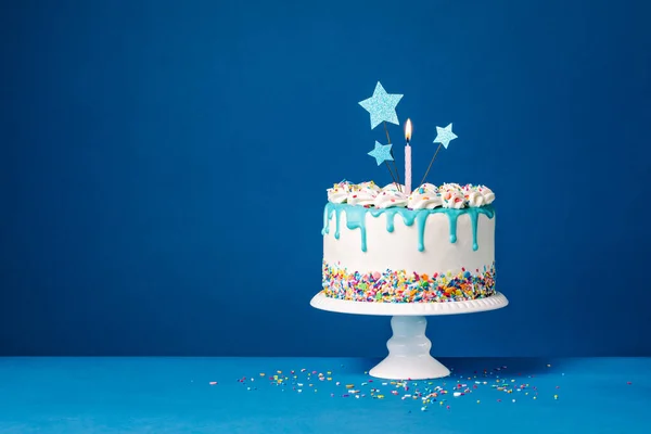 白色的生日蛋糕 上面有三颗星星 一支蜡烛和五彩斑斓的彩灯洒在蓝色的背景上 复制空间 — 图库照片