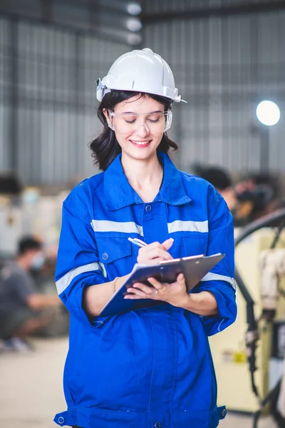 エンジニア女性整備士は クリップボード上のチェックリストを保持し 製鉄所のワークショップでペン 自動製造技術のための産業用ロボットプログラミングソフトウェア ロイヤリティフリーのストック画像