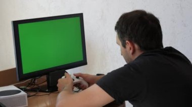 Young male gamer playing game console using joystick remote control over green screen monitor tv chroma key at home. Man Focused Gaming in Living Room