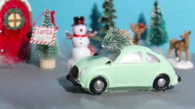 Yeni yıl ya da Noel durağı animasyonu. Çatıda Noel ağacı olan şirin bir oyuncak araba caddeden aşağı doğru gidiyor, evlerin önünde duruyor ve pencerelere ışık saçıyor..