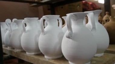 Seramik fabrikasında bir sürü kil ya da beyaz seramik vazo, sürahi ve kap kacak var. Seramik tabaklar henüz fırından çıkmamış..