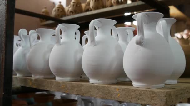 在陶瓷制造厂的摊位上 有许多人造的粘土或白色陶瓷花瓶 壶和器皿 陶瓷餐具还没有从烤箱上画出来 — 图库视频影像