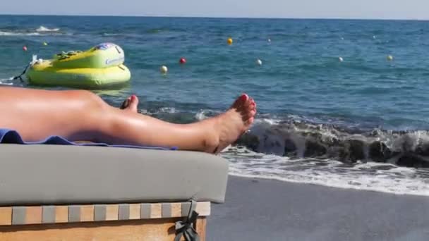 ギリシャのヘルソニソス 2022年7月13日 海の波の揺れを背景にビーチで日光浴デッキチェアに赤いペディキュアを持つ女性の足 夏休み海による休暇リラックス — ストック動画