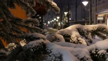 Bir kış akşamı ya da gece sokakta karla kaplı ladin dalları. Sokakları Noel aydınlatması. Görüntüyü kapat.