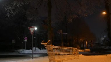 Karanlık bir kış akşamında fenerlerin ışığında sokaktaki bir süpermarketten boş bir el arabası..