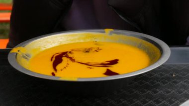 Kabak çekirdeği ve soya soslu kabak kremalı çorba. Bir adam sokakta metal bir tabaktan çorba içiyor..