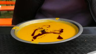 Kabak çekirdeği ve soya soslu kabak kremalı çorba. Bir adam sokakta metal bir tabaktan çorba içiyor..