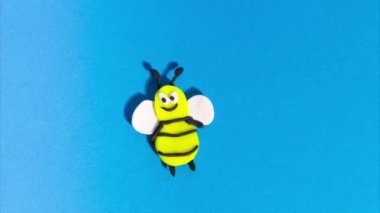 Stop motion animation from plasticine. Cheerful funny bee flying on a blue background. Claymotion cartoon.