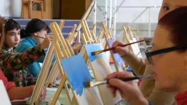 KEHL, ALMANY - 4 Mart 2023: Bir grup yetişkin ve çocuk tuvallere resim yapmayı öğreniyor. Masada bir sürü farklı boya ve fırça var. Çizim dersleri