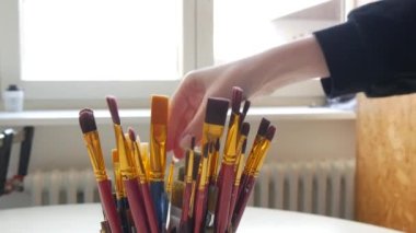 Bir kadın sanatçı el, bir sanat stüdyosundaki diğer profesyonel fırçalardan bir boya fırçası alır..