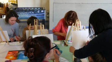 KEHL, ALMANY - 4 Mart 2023: Bir grup yetişkin ve çocuk tuvallere resim yapmayı öğreniyor. Masada bir sürü farklı boya ve fırça var. Çizim dersleri