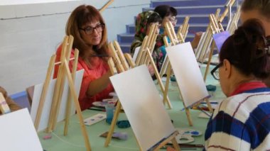 KEHL, ALMANY - 4 Mart 2023: Bir grup yetişkin ve çocuk tuvallere resim yapmayı öğreniyor. Masada bir sürü farklı boya ve fırça var. Çizim dersleri