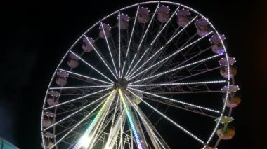 Gece gökyüzünün arka planına karşı büyük renkli bir dönme dolap. Dönme dolap rengarenk bir gece, dışarıdaki rotasyon parkı, yıllık tapınak etkinliği...
