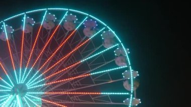 Gece gökyüzünün arka planına karşı büyük renkli bir dönme dolap. Dönme dolap rengarenk bir gece, dışarıdaki rotasyon parkı, yıllık tapınak etkinliği...
