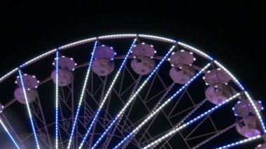 Gece gökyüzünün arka planına karşı büyük renkli bir dönme dolap. Dönme dolap rengarenk bir gece, dışarıdaki rotasyon parkı, yıllık tapınak etkinliği...