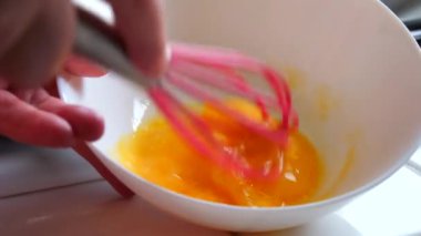 Bir kadın özel bir silikon çırpıcıyla yumurtayı kırbaçlıyor. Yavaş çekimde ev yapımı çörekler yapıyor..