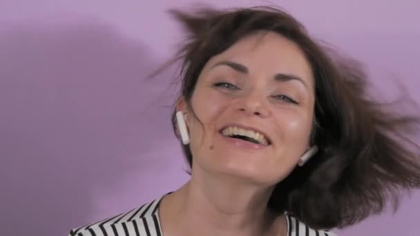 ワイヤレスヘッドフォンやダンス 歌を聴く若い陽気な女性の肖像画 紫色の背景にある女性の感情 ゆっくりとした動き — ストック動画