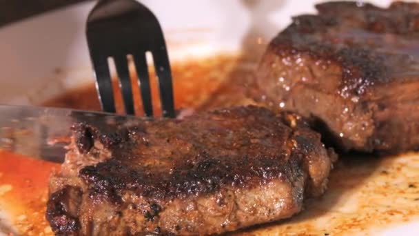 プレートに焼き上げたビーフステーキの大きな部分 スローモーションで血液を含む中東ロースト肉 ナイフとフォークが一片を閉じたビューをカット — ストック動画