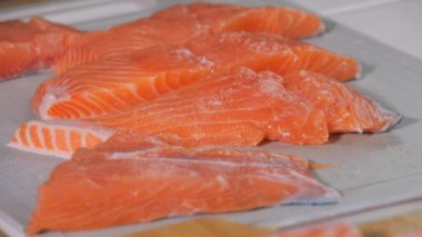 Bir parça taze kırmızı balık yavaş çekimde yakın çekim görüntüsüyle tuz serpiştirilir. Baharatlı somon bifteği. Aşçı pişirmeden önce çiğ bifteğe baharat ekliyor..