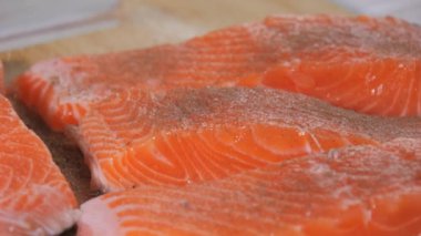 Bir parça taze kırmızı balık yavaş çekimde siyah biber serpiştirilir. Baharatlı somon bifteği. Aşçı pişirmeden önce çiğ bifteğe baharat ekliyor..