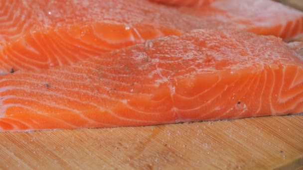 新鮮な赤い魚の部分は スローモーションの近くのビューで地面の黒唐辛子で振られています サーモンステーキの味付け 焼く前に生ステーキにスパイスを加えるシェフ — ストック動画