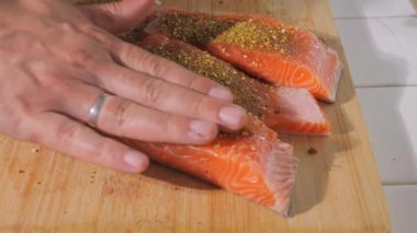 Bir parça taze kırmızı balık yavaş çekimde tuz ve baharatlarla serpiştirilir. Baharatlı somon bifteği. Şef pişirmeden önce bifteği elleriyle ovuyor..