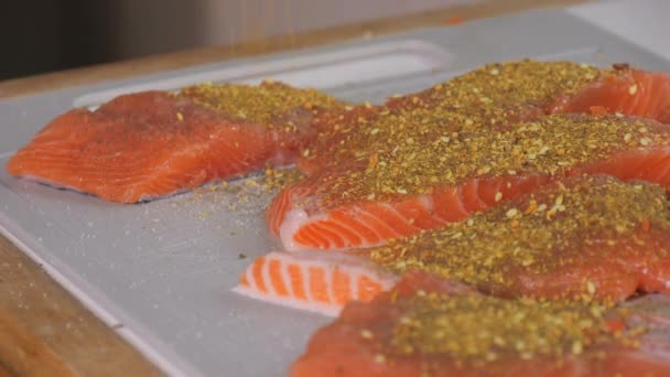 新鮮な赤い魚の断片は スパイスと塩でスパイスで振られ スローモーションが近づいています サーモンステーキの味付け 焼く前に生ステーキにスパイスを加えるシェフ — ストック動画