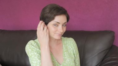 Yeşil gözlü ve kısa saçlı güzel bir kadın. Kameraya bakar, saçına dokunur ve ağır çekimde gülümser..