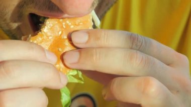 Sarı tişörtlü genç bir adam iştahlı bir hamburger ya da burger yer. Ağız yavaş çekimde kapanır. Abur cuburları ısırıp çiğniyorlar..