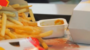 Bir adam patates kızartmasını fast food restoranında sosa batırır. Çöp, yağlı yiyecekler..