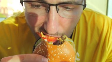 Sarı tişörtlü genç bir adam iştahlı bir hamburger ya da burger yer. Ağzını kapat. Abur cuburları ısırıp çiğniyorlar..
