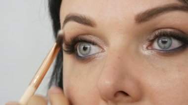 Güzel bir genç kadın, profesyonel bir makyajcı tarafından göz makyajı yapmak için özel bir fırçayla güzellik stüdyosunda şık bir akşam makyajı yapıyor...