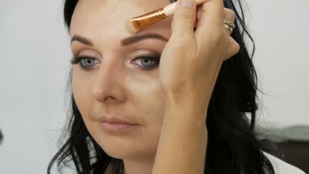 여자는 그녀의 얼굴에 컨실러를 브러시 스폰지를 스튜디오에서 메이크업 아티스트에 메이크업을 — 비디오