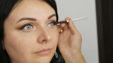 Güzel bir genç kadın, profesyonel bir makyajcı tarafından göz makyajı yapmak için özel bir fırçayla güzellik stüdyosunda şık bir akşam makyajı yapıyor...