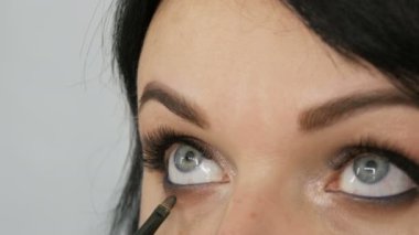 Güzel bir genç kadın, profesyonel bir makyajcı tarafından göz makyajı yapmak için özel bir fırçayla güzellik stüdyosunda şık bir akşam makyajı yapıyor...