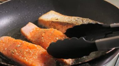 Baharatlı taze kırmızı balık filetosu. Somon fileto eti tavada ayçiçeği yağında kızartılır, mutfak maşası bir parça döner, yakın çekim, yavaş çekim..